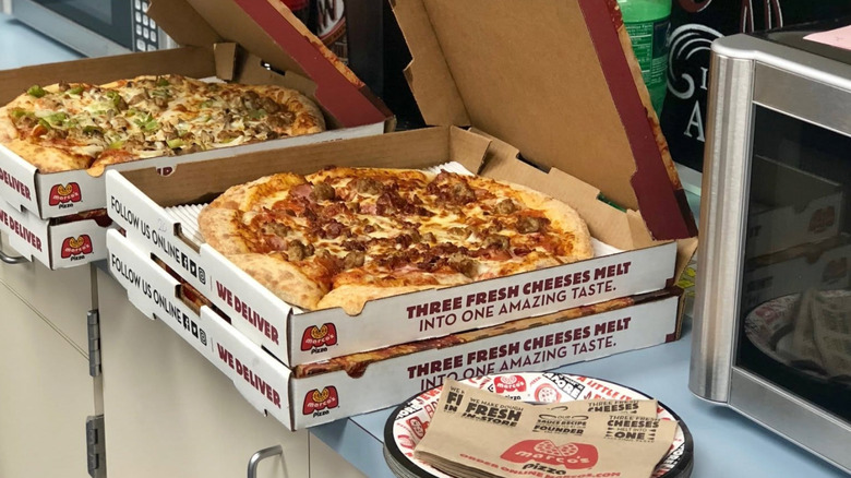 Pizza sits in boxes in stacks on a counter.
