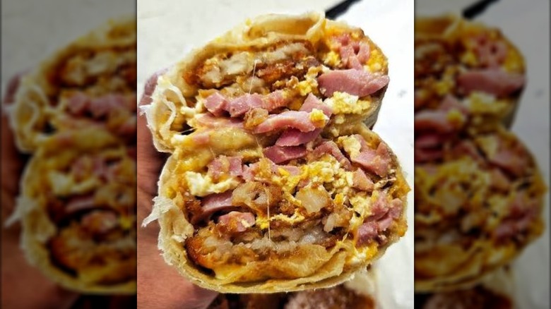 A hand holding up both halves of a build-your-own breakfast burrito.