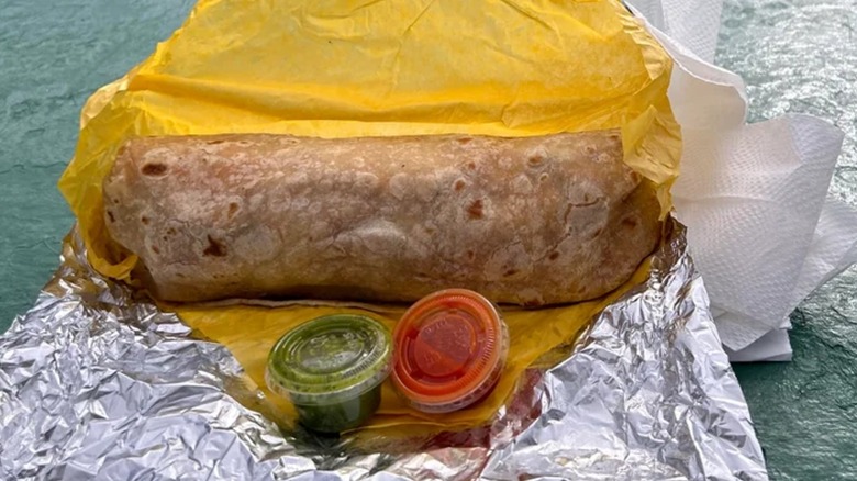 A Humberto's breakfast burrito with green and red salsa on a picnic table.