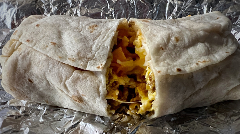 A breakfast burrito cut in half on a sheet of tinfoil.