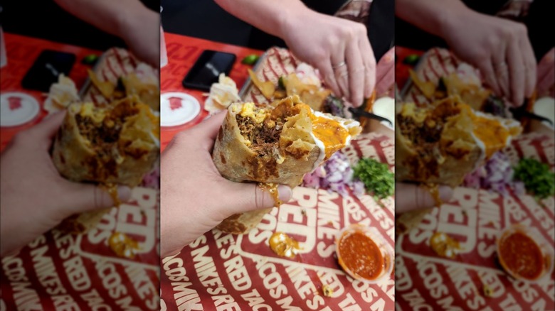 A hand holding a breakfast birria burrito against a Mike's Red Taco paper-lined tray.
