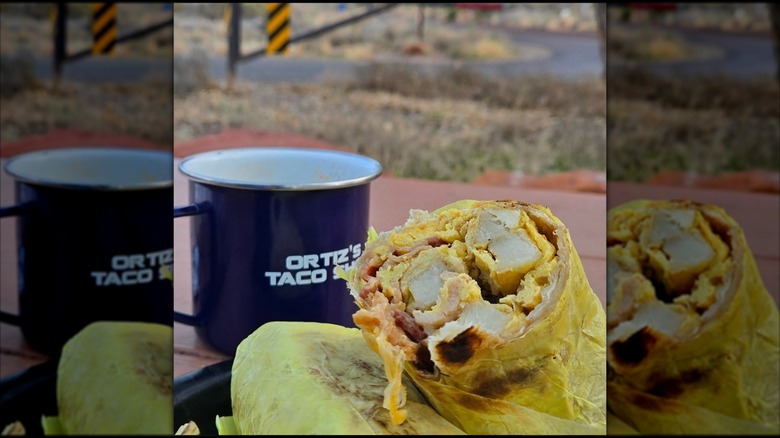 A breakfast burrito next to an Ortiz's Coffee Shop coffee cup on a picnic table.