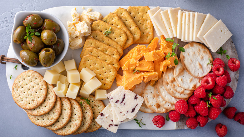 cheese plate with cheese slices, crackers, raspberries, and olives