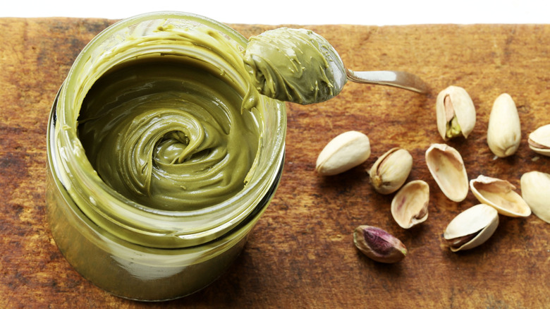 A spoonful and jar of pistachio paste next to pistachios.