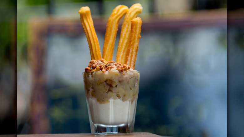 Churros sticking out of a cup of banana pudding topped with nuts.