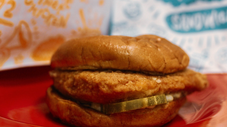 Closeup of Popeyes fish sandwich resting in front of takeout bags
