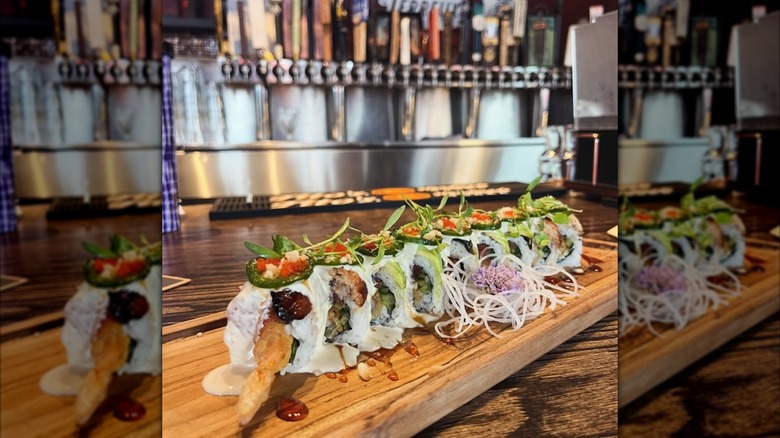 Sushi roll on cutting board on a bar in front of beer taps