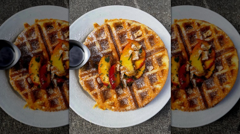 Waffles covered with peaches and powdered sugar on a white plate.