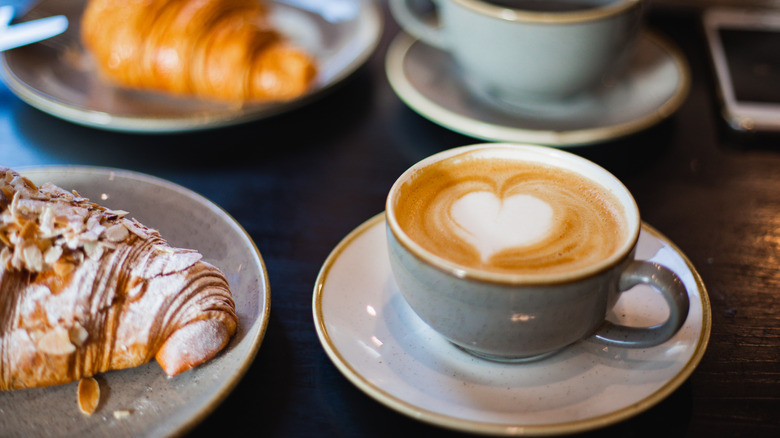 Croissants and coffee cup with latte art on saucers.