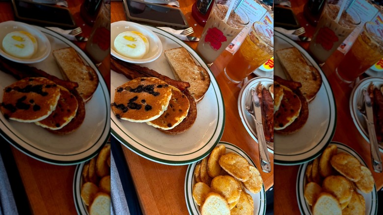 Plate of blueberry pancakes, toast, bacon and an iced coffee in a glass cup.