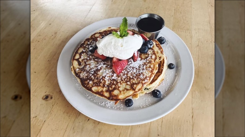 Plate of pancakes with strawberries, blueberries, whipped cream, and maple syrup.