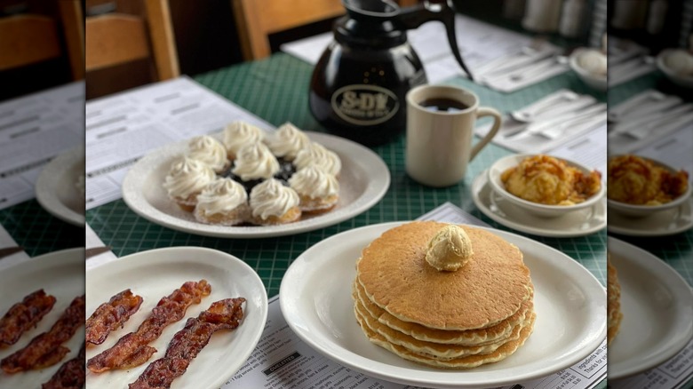 Bacon, pancakes, and other breakfast foods on white plates.
