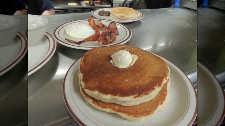Pancakes, eggs, and bacon on white plates.