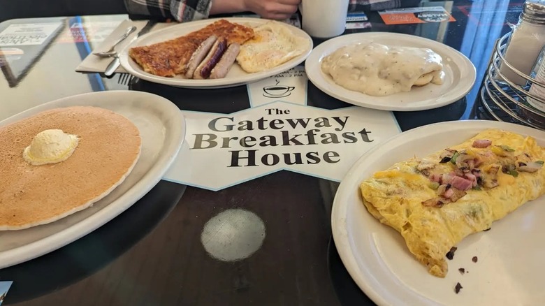 Pancakes with butter, sausage links, and omelettes on white plates.