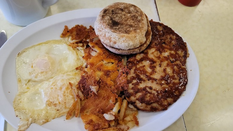 Eggs, hash browns, an English muffin, and breakfast sausage patties on a white plate.