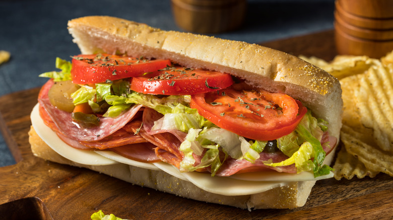 Italian sub on cutting board beside potato chips