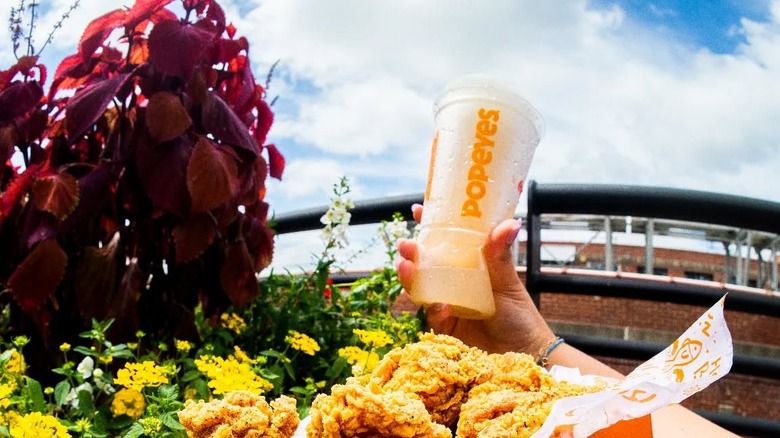 A hand holds up a Popeyes drink.