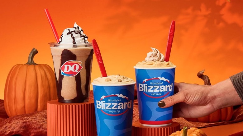 Blizzards and an iced coffee sit arranged near a pumpkin.