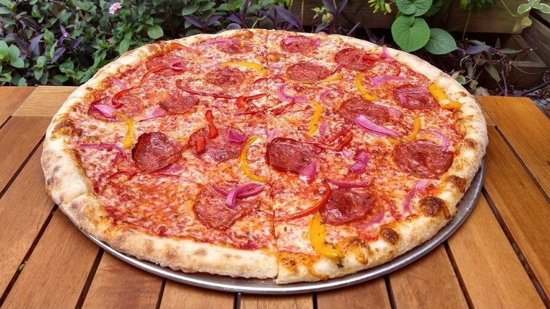 Pizza Delicious pepperoni, pepper, and onion pie on outdoor table