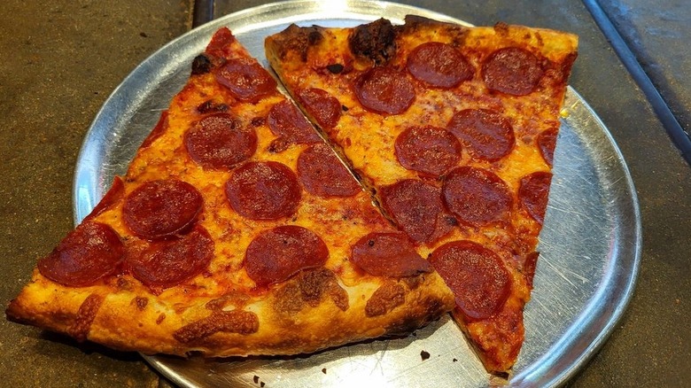 Two slices of thin crust pepperoni pizza sit on a metal plate at Pizza Delicious