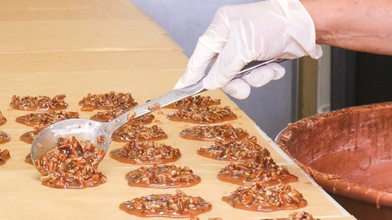 Gloved hand spooning praline mix onto parchment paper