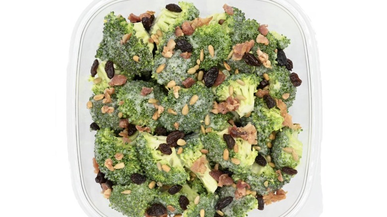 Plastic to-go container of broccoli salad topped with smoked bacon and roasted sunflower seeds