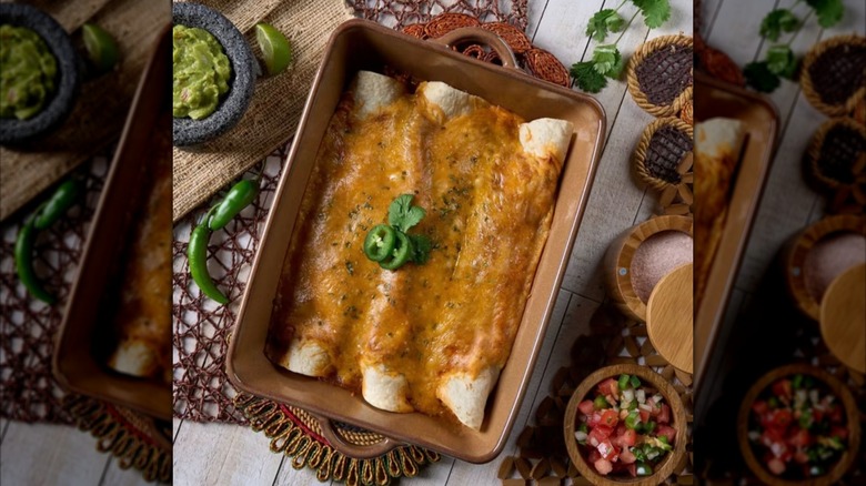 Tray of Member's Mark Rotisserie Chicken Enchiladas garnished and surrounded by bowls of guacamole and pico de gallo