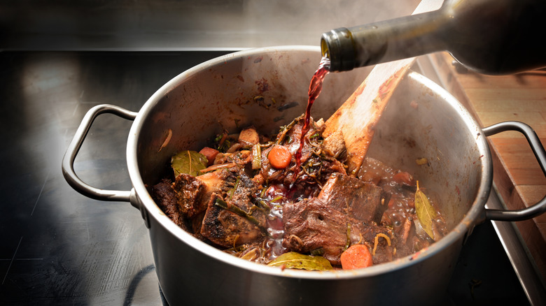 Chef pours red wine into a pot of beef and vegetables