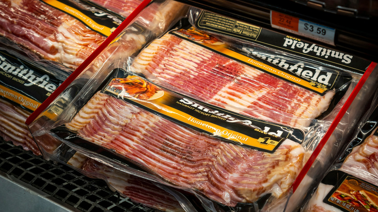 A person holds a pack of Smithfield smoked sausage by a grocery store display case