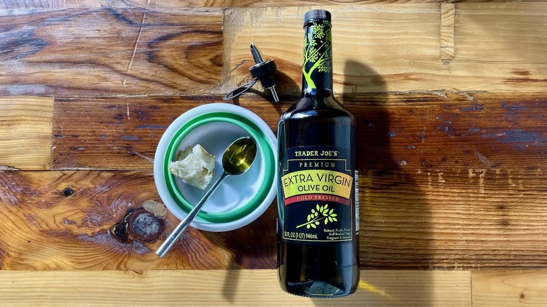 Overhead view of a bottle of Trader Joe's Premium Extra Virgin Olive Oil lying on a wooden table with a spoonful of the oil and a piece of bread