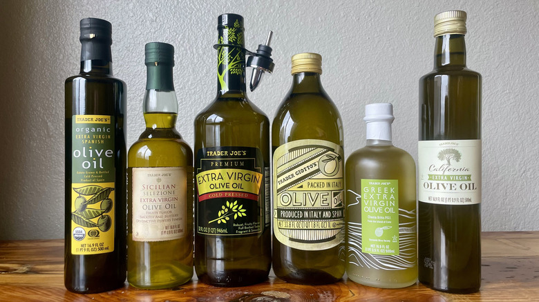 Six different types of Trader Joe's Olive Oil lined up on a wooden table