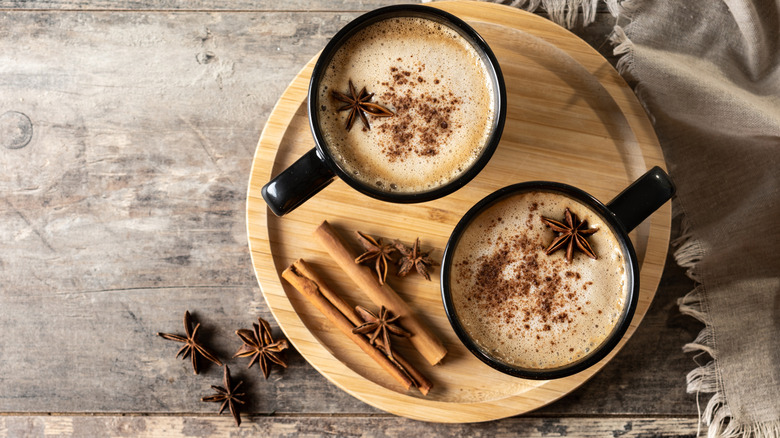 Two cups of chai surrounded by cinnamon and star anise