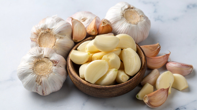 Bowl of fresh garlic cloves surrounded by heads of garlic