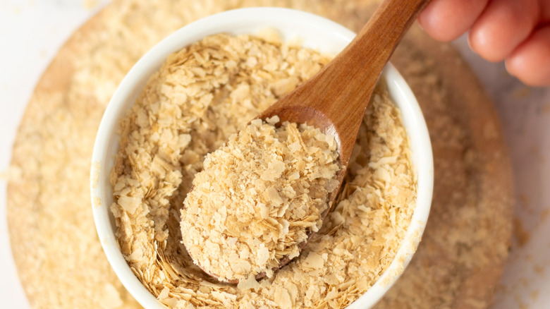 Hand holding spoonful of nutritional yeast over a jar of it