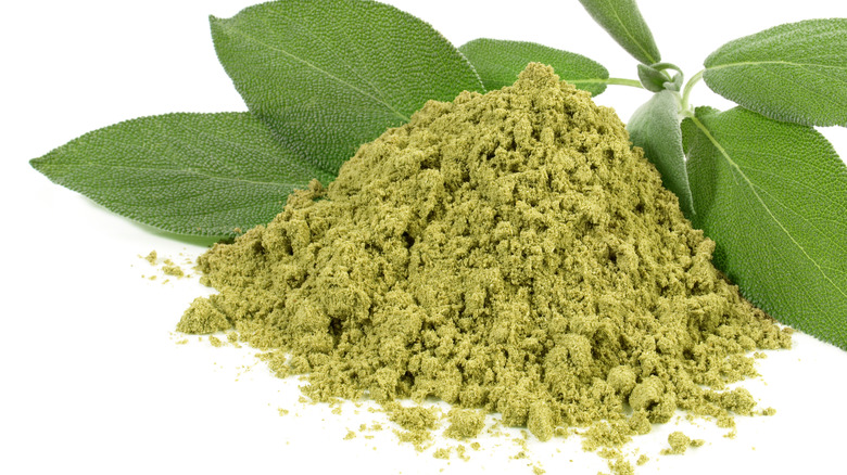 Pile of sage powder surrounded by fresh sage leaves
