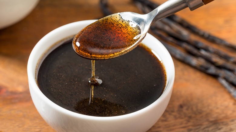 Bowl and spoonful of vanilla extract with pods in the background