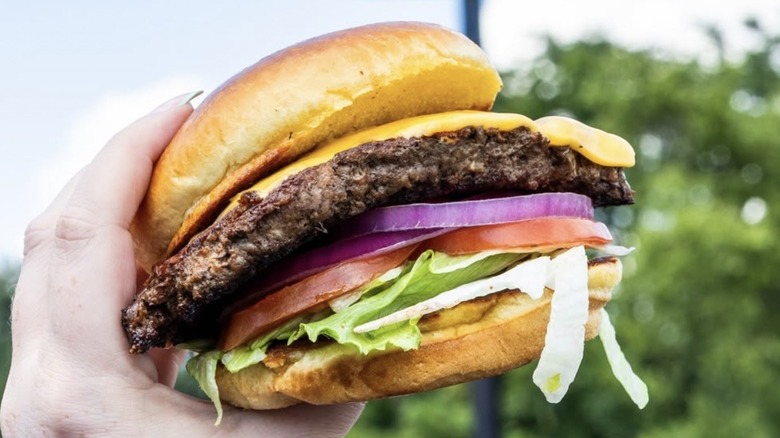 Hand holding a Texas Roadhouse All-American Cheeseburger outside a restaurant