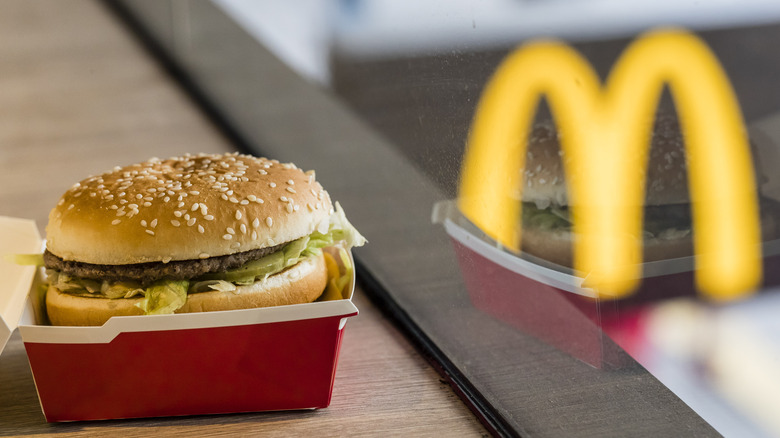 Big Mac in a box next to a reflection of the McDonald's logo in the window