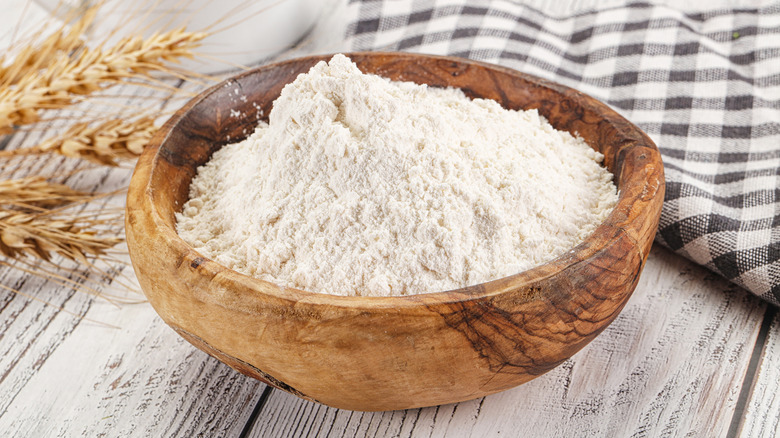 a wooden bowl of flour resting in a pile of flour in a kitchen