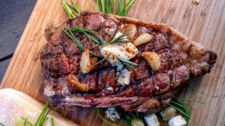A ribeye steak is topped with fresh herbs, roasted garlic, and a pat of butter.