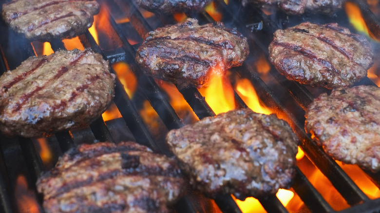Closeup of hamburger patties grilling over open flames