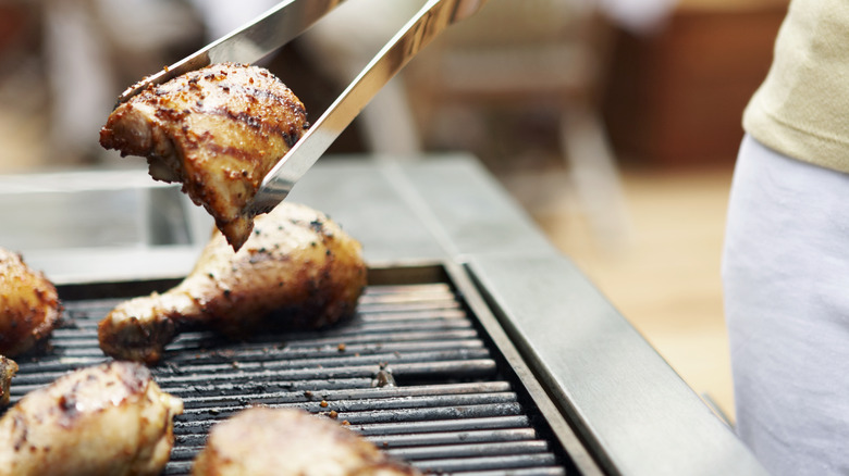 Grilling tongs flipping a grilled chicken thigh