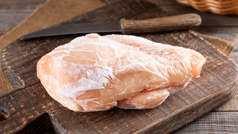 Frozen chicken fillet on a cutting board next to a knife