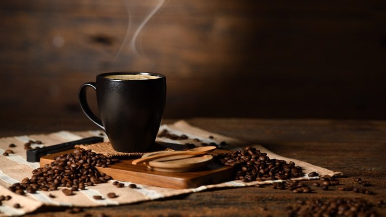 cup of hot coffee and coffee beans on wooden table