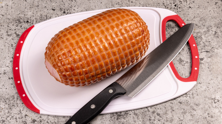 A boneless, mini ham on a cutting board with a knife.