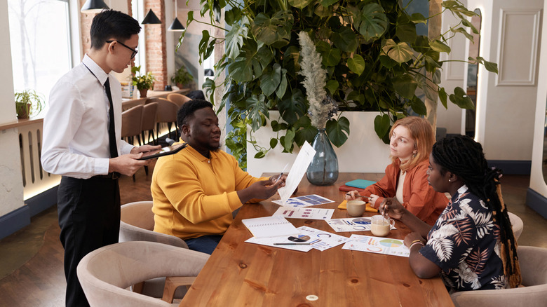 Young server bringing food to three friends or coworkers at a restaurant.