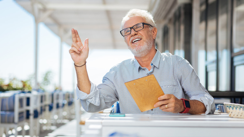 An older diner holds the bill and tries to get a server's attention.