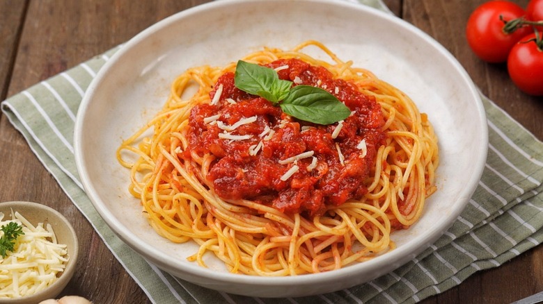 A white bowl of spaghetti topped with tomato sauce and basil leaves