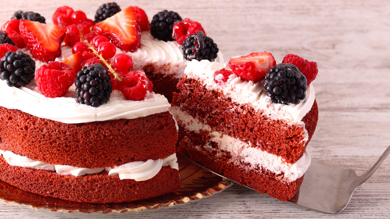A slice taken out of a red velvet cake topped with berries.