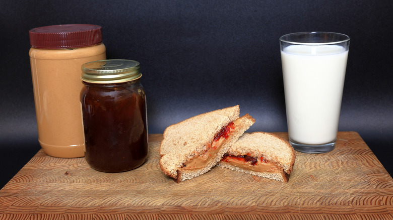 Jars of peanut butter and jelly next to a PB&J and a glass of milk